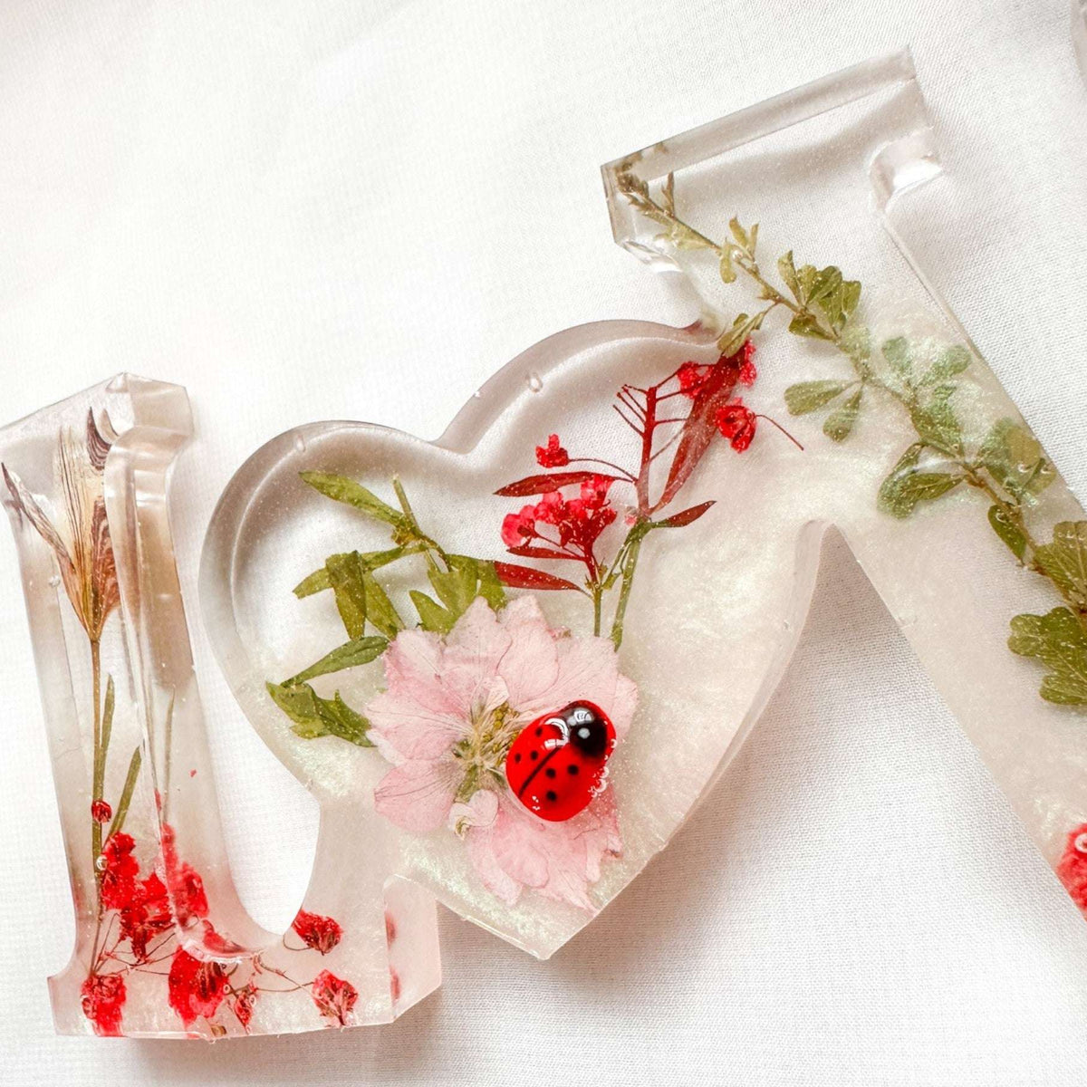 Close-up of real foraged garden greenery and red ladybug charms in resin