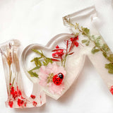 Close-up of real foraged garden greenery and red ladybug charms in resin