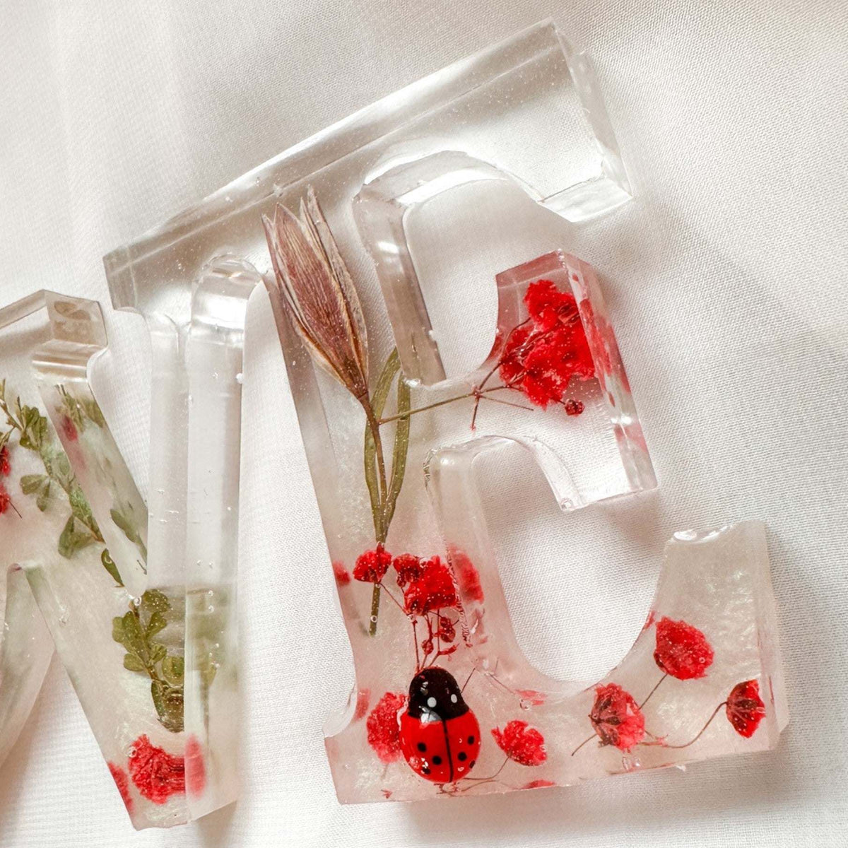 Close-up of real foraged garden greenery and red ladybug charms in resin