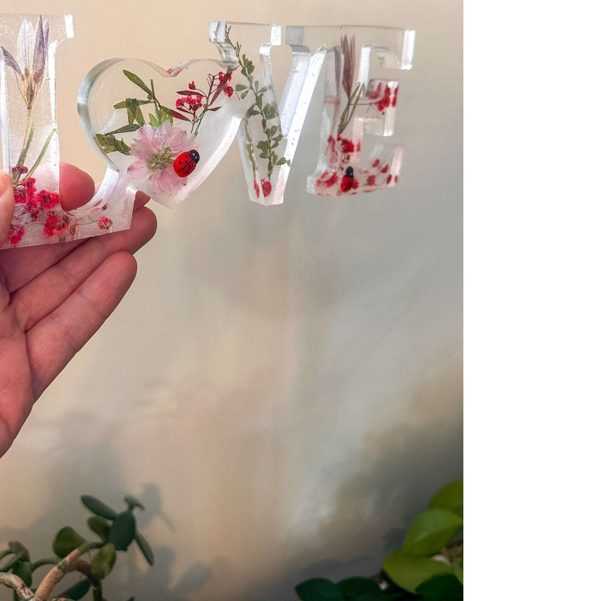 Close-up of real foraged garden greenery and red ladybug charms in resin