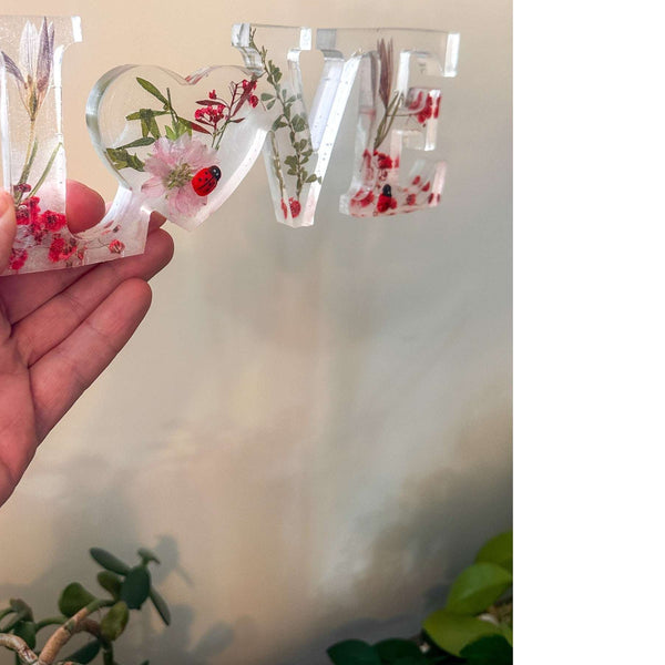 Close-up of real foraged garden greenery and red ladybug charms in resin