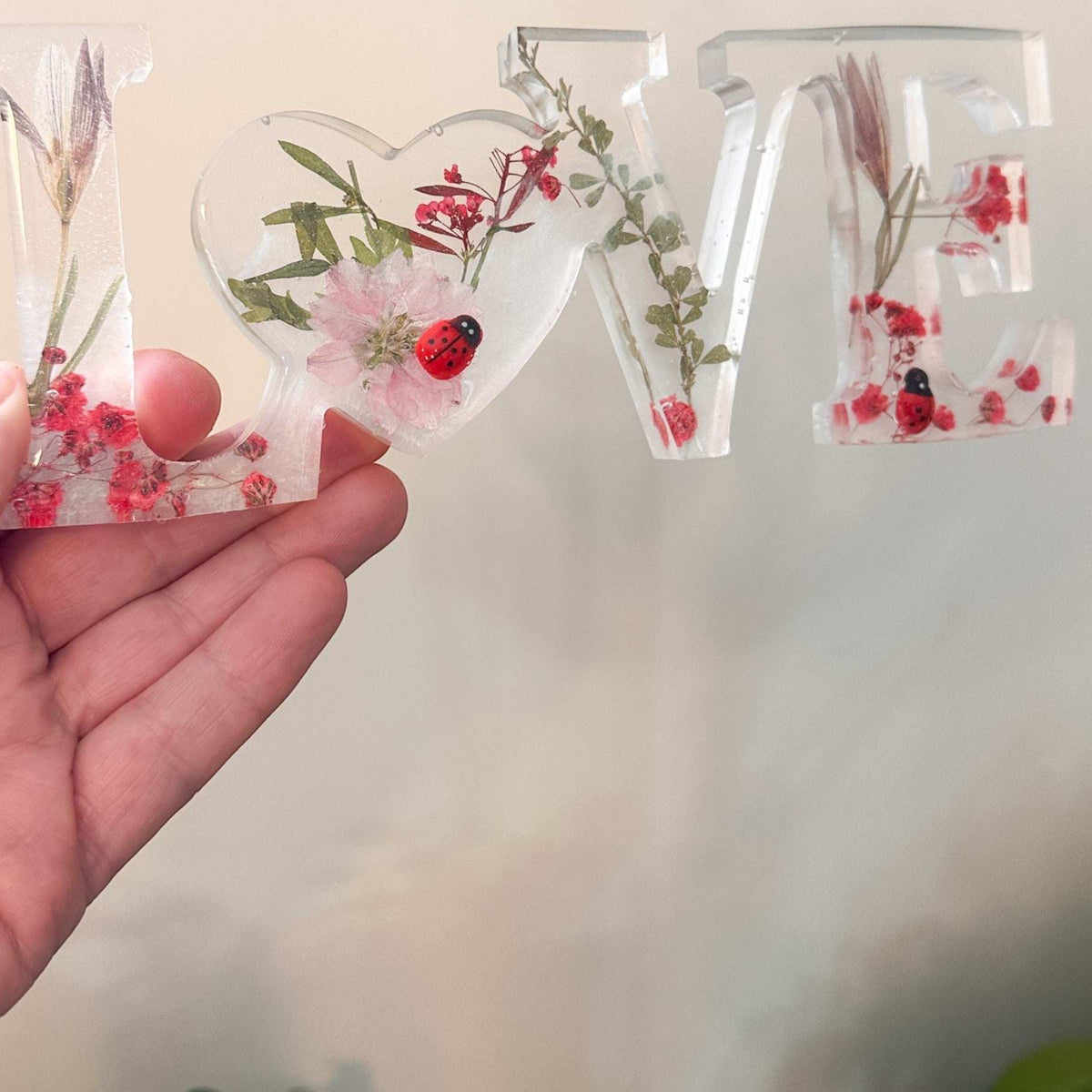 Close-up of real foraged garden greenery and red ladybug charms in resin