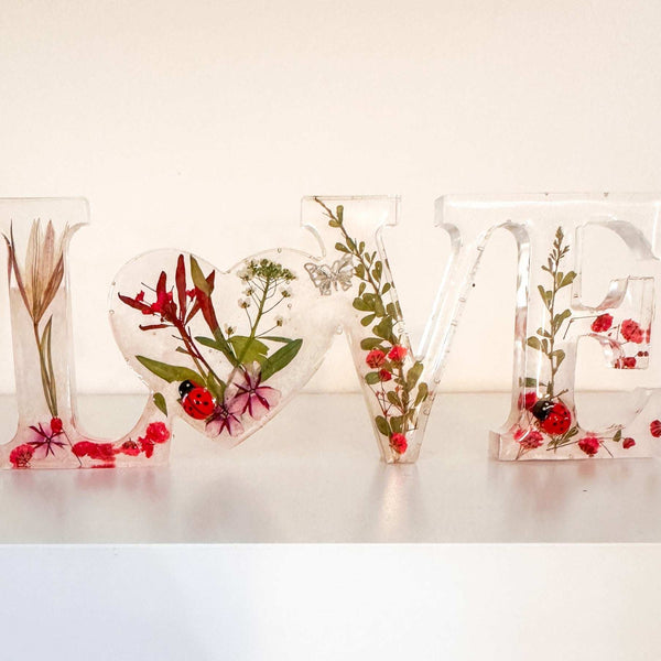 Close-up of real foraged garden greenery and red ladybug charms in resin
