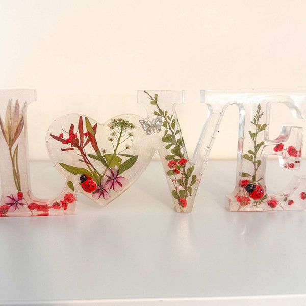 Close-up of real foraged garden greenery and red ladybug charms in resin