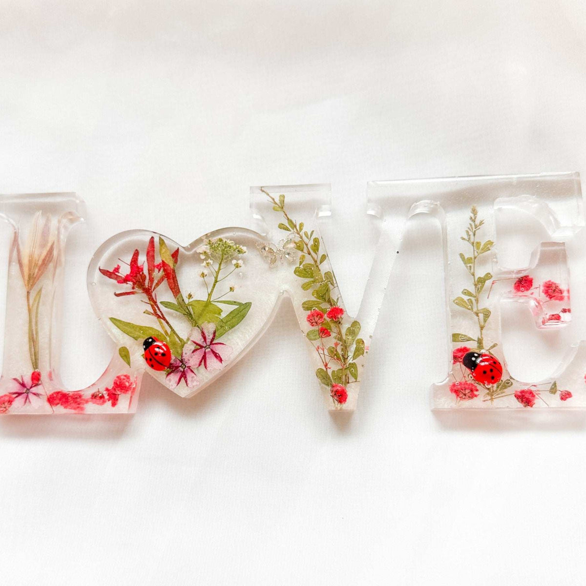 Close-up of real foraged garden greenery and red ladybug charms in resin