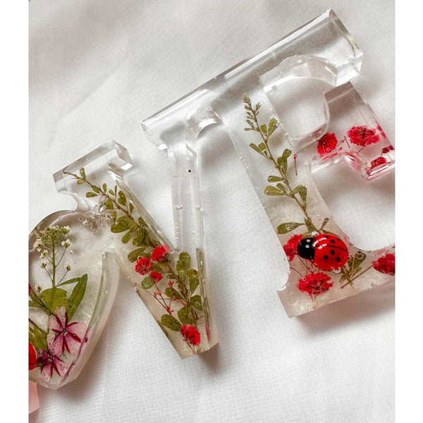 Close-up of real foraged garden greenery and red ladybug charms in resin