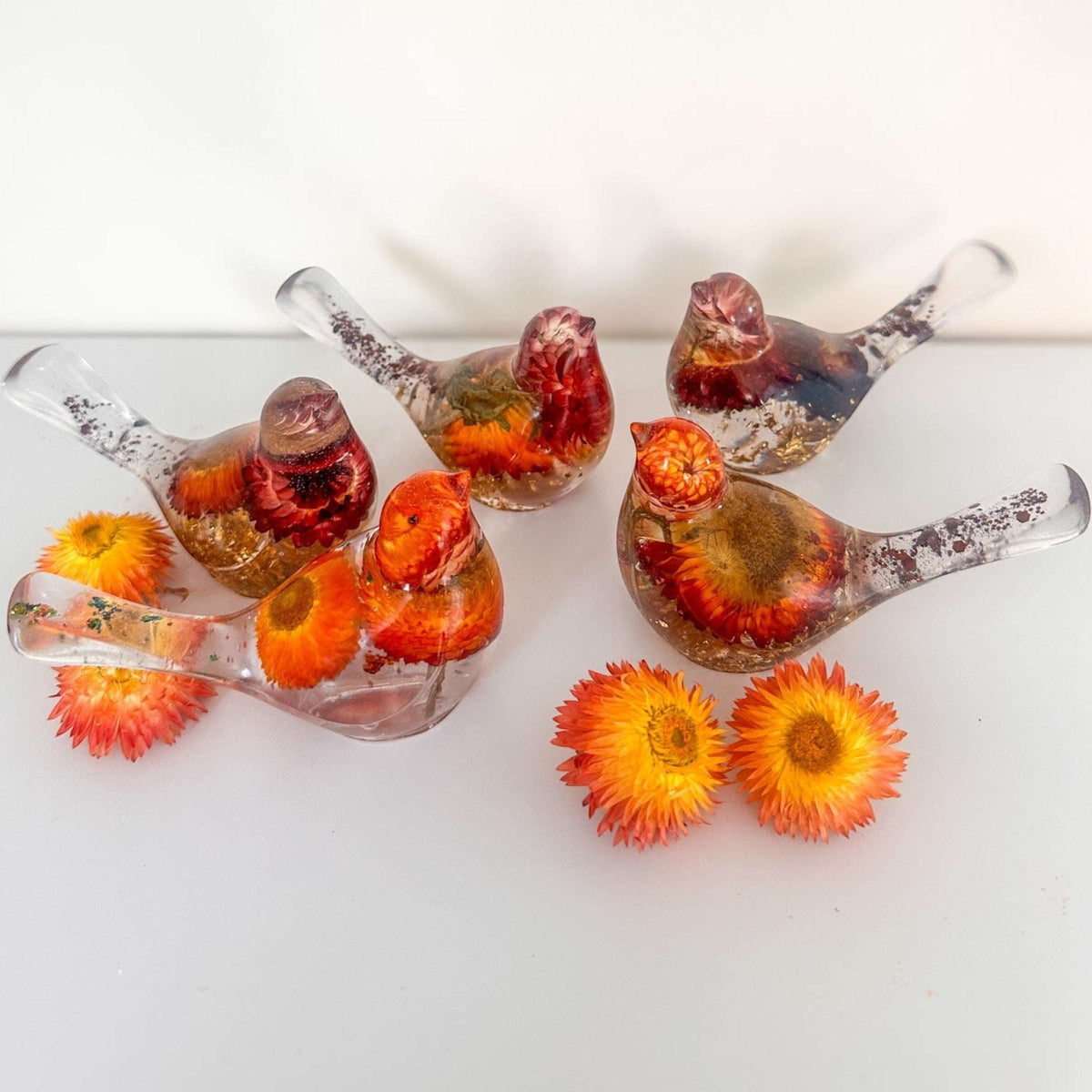 Harvest Songbird strawflower resin bird decor perched on a shelf with loose dried strawflowers