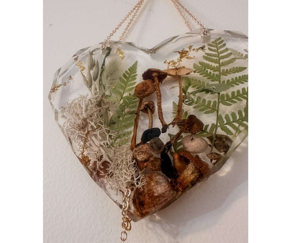 Close-up of real foraged mushrooms and ferns preserved in clear gold leaf resin heart suncatcher