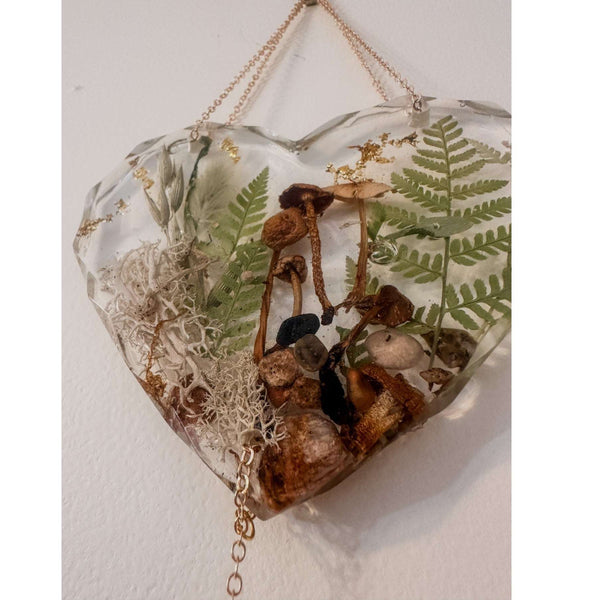 Close-up of real foraged mushrooms and ferns preserved in clear gold leaf resin heart suncatcher