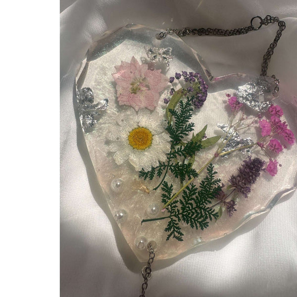 Close-up of silver cubic zirconia butterfly and real pressed pink daisy preserved in clear resin heart suncatcher