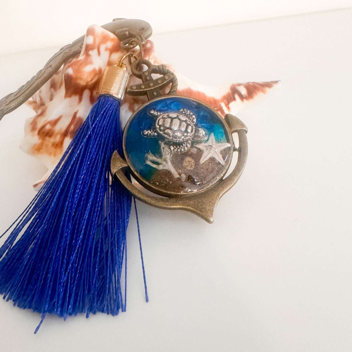 Close-up of real sand, starfish and ocean blue resin preserved inside anchor shaped bookmark charm