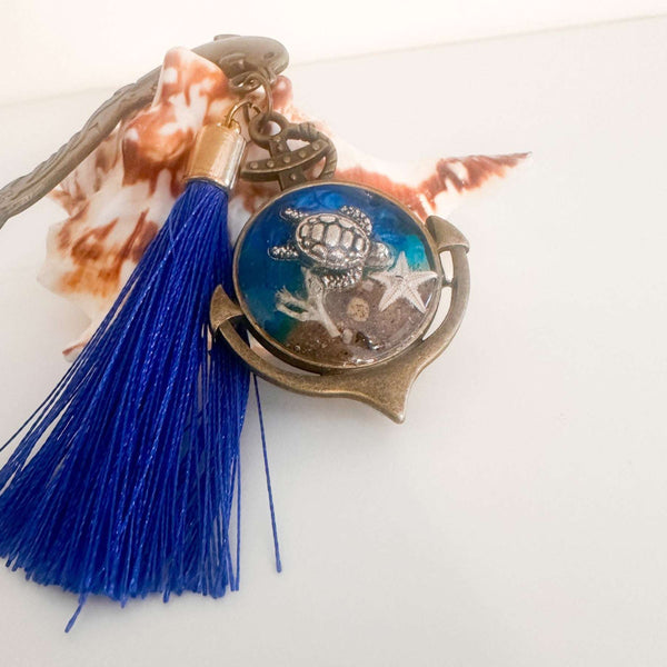 Close-up of real sand, starfish and ocean blue resin preserved inside anchor shaped bookmark charm