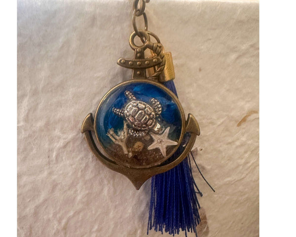 Close-up of real sand, starfish and ocean blue resin preserved inside anchor shaped bookmark charm
