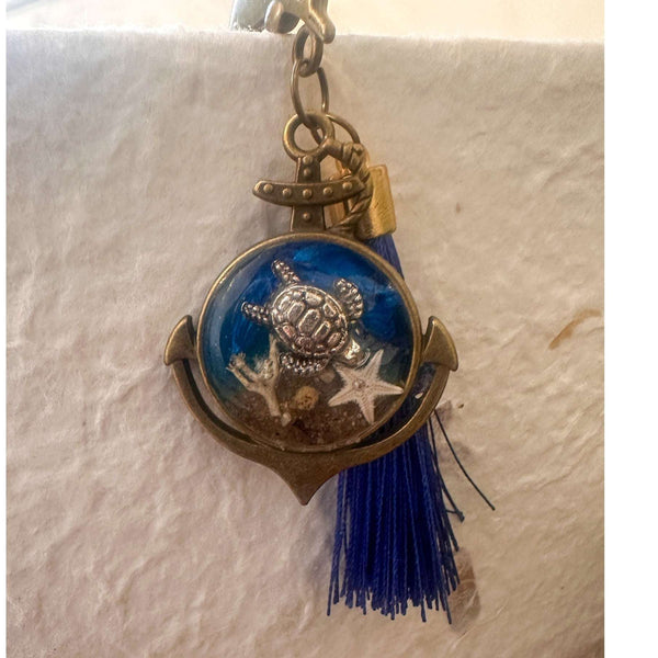 Close-up of real sand, starfish and ocean blue resin preserved inside anchor shaped bookmark charm