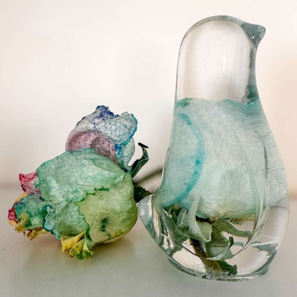Blue Rose Songbird rainbow rose resin bird decor beside a real rainbow rose on a soft lit surface