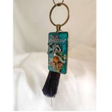 Handmade teal resin keychain with a silver fairy on real Boreal forest mushrooms and white wildflowers, brown tassel and antique copper hardware, white background.