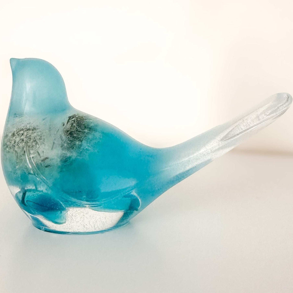 Close-up of real dandelion seeds suspended in deep teal hand-poured resin bird decor