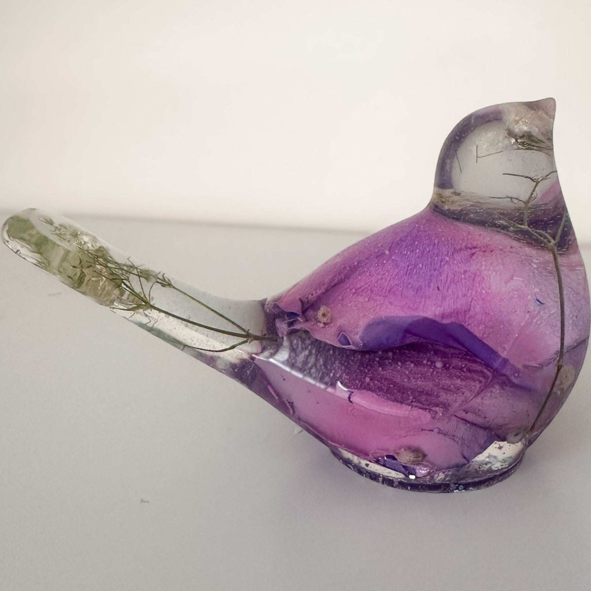 Close-up of soft purple and pink rainbow rose petals suspended in clear hand-poured resin bird figurineClose-up of soft purple and pink rainbow rose petals suspended in clear hand-poured resin bird figurine