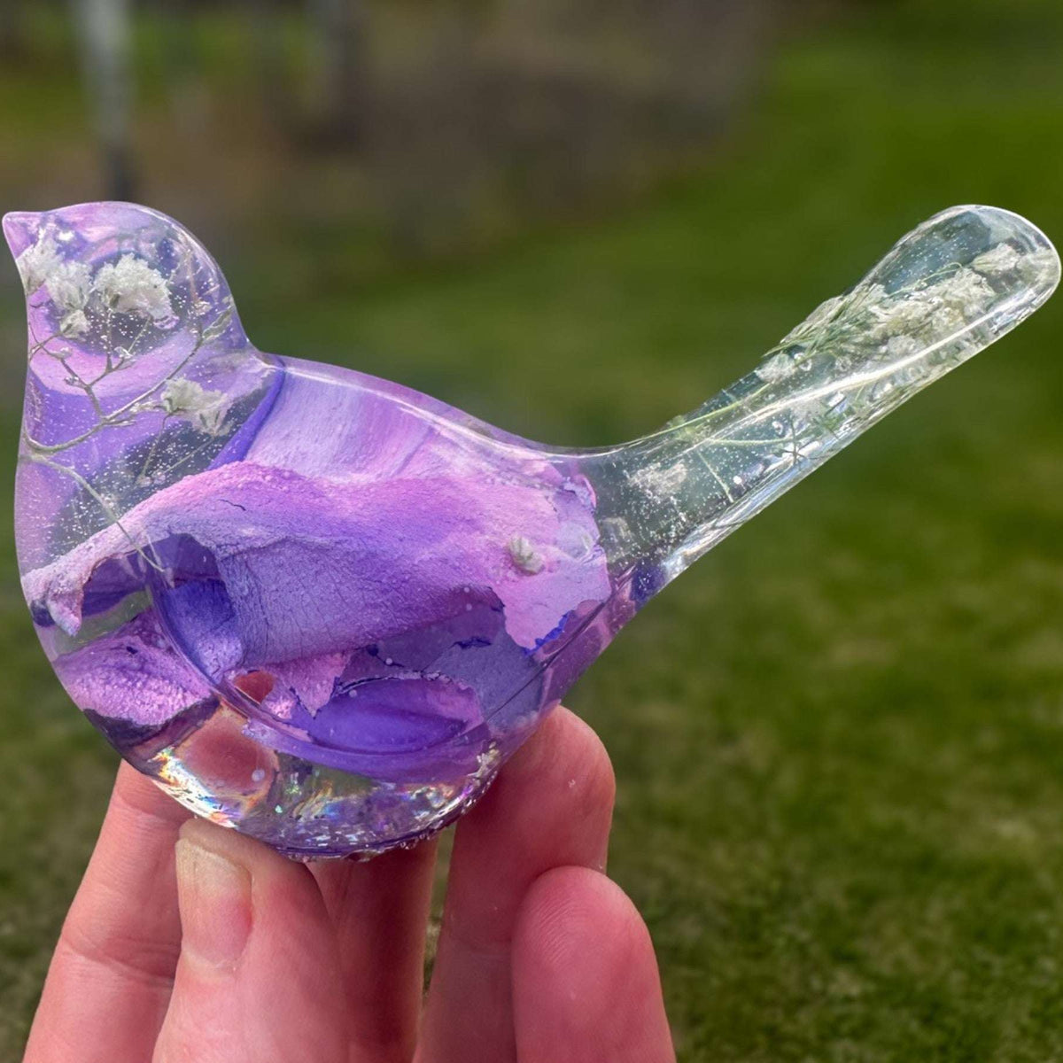 Close-up of soft purple and pink rainbow rose petals suspended in clear hand-poured resin bird figurine