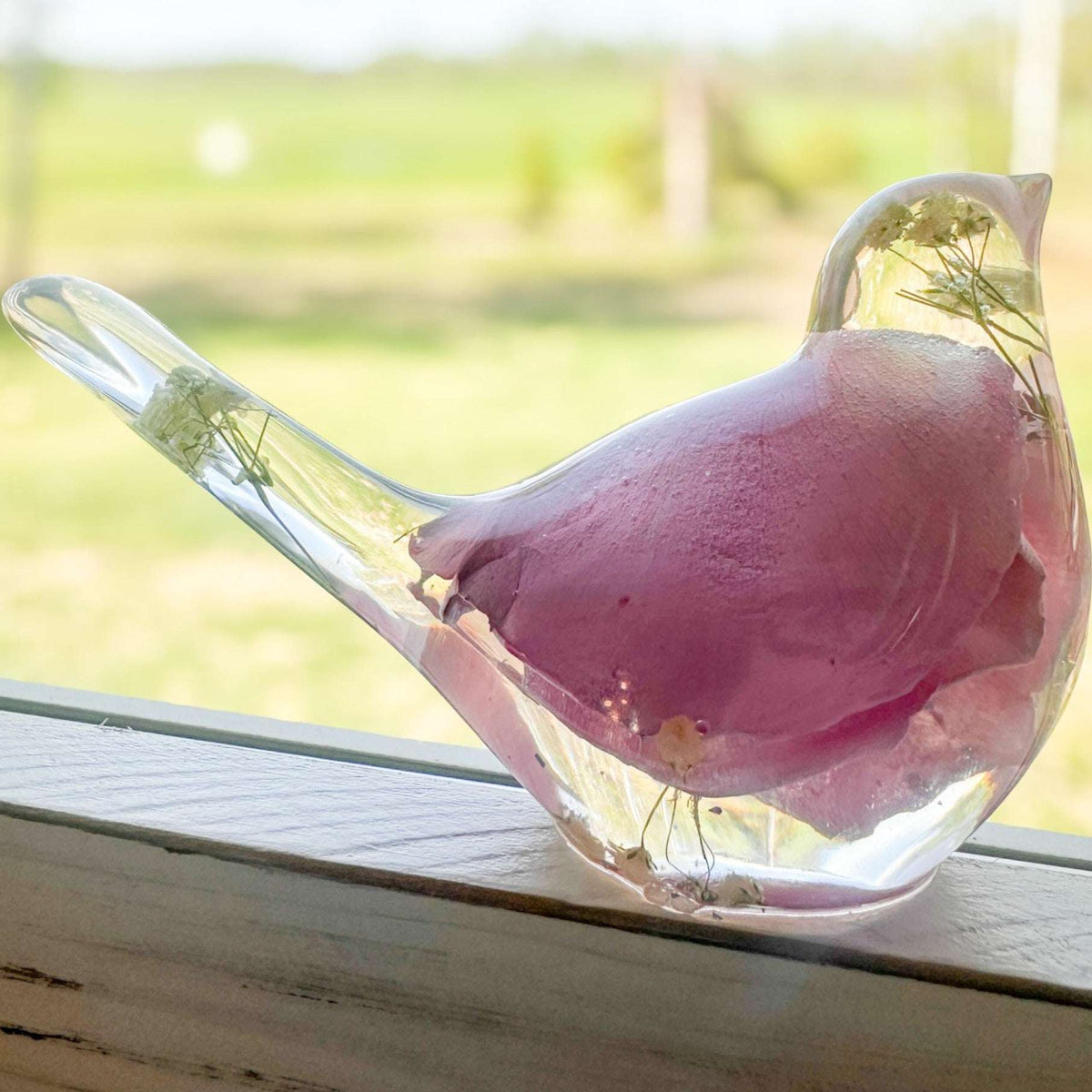 Close-up of a soft pink rose petal and white baby's breath suspended inside clear hand-poured resin bird figurine