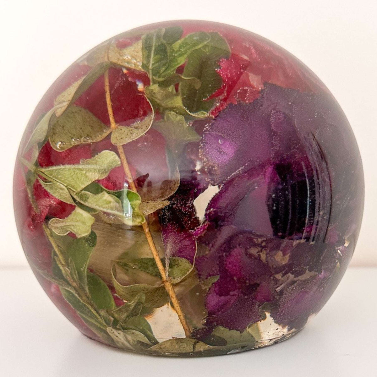 Handcrafted floral resin sphere with real dark pink and purple carnations and LED base glowing as a decorative garden nightlight