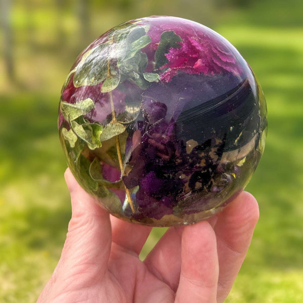 Handcrafted floral resin sphere with real dark pink and purple carnations and LED base glowing as a garden nightlight