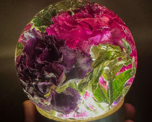 Handcrafted floral resin sphere with dark pink and purple carnations and LED light base glowing as a decorative garden centerpiece