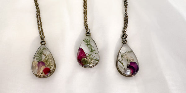 Three teardrop-shaped necklaces with embedded flowers on a white background