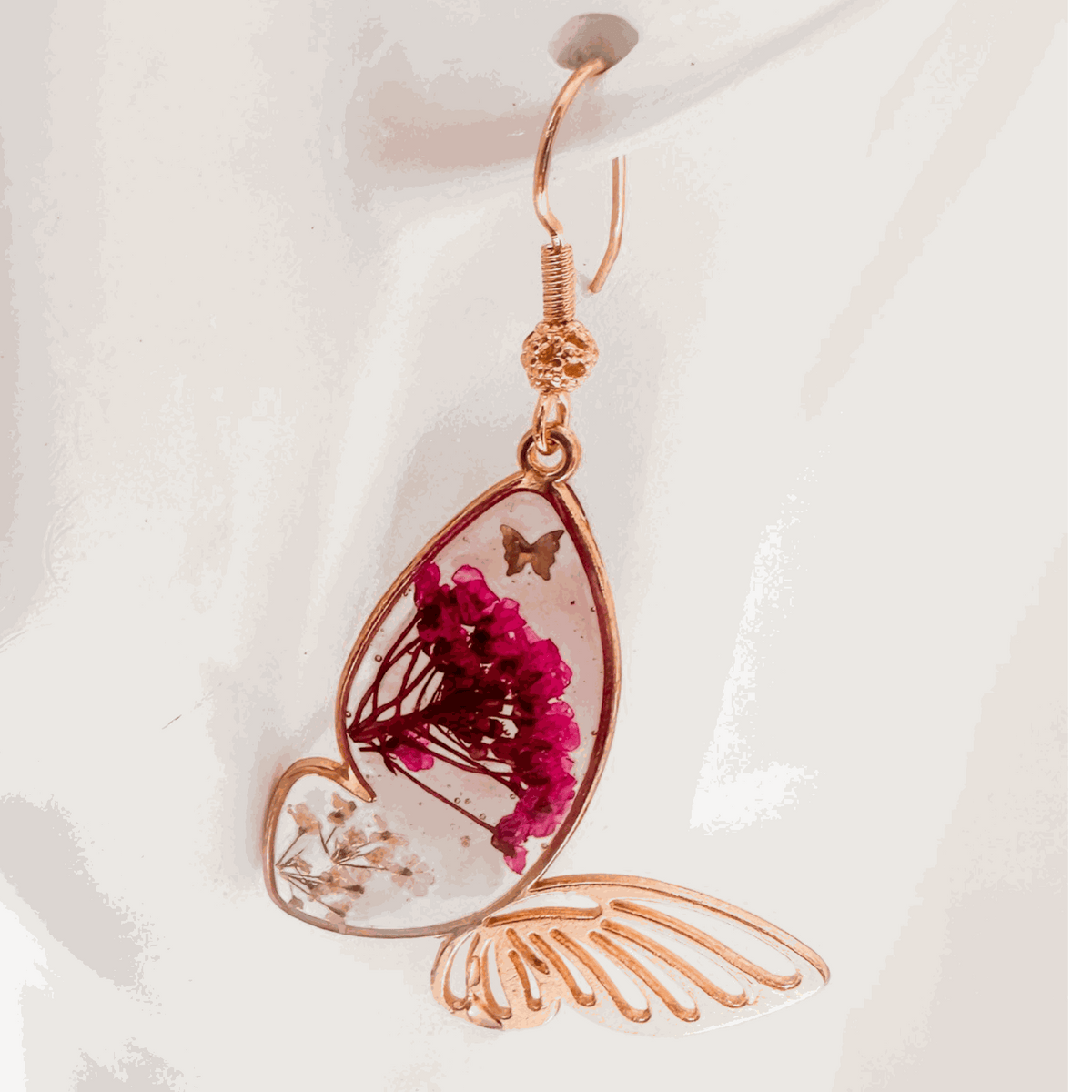 Rose gold Garden Wing Earrings with pressed deep pink and white flowers in resin butterfly wings and gold butterfly accent