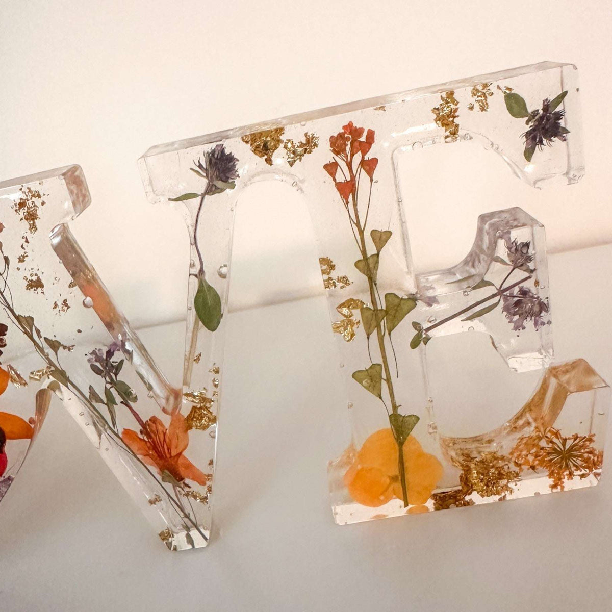 Pressed flower resin decor featuring LOVE word art with real orange and red wildflowers and a tiny ladybug in clear resin letters