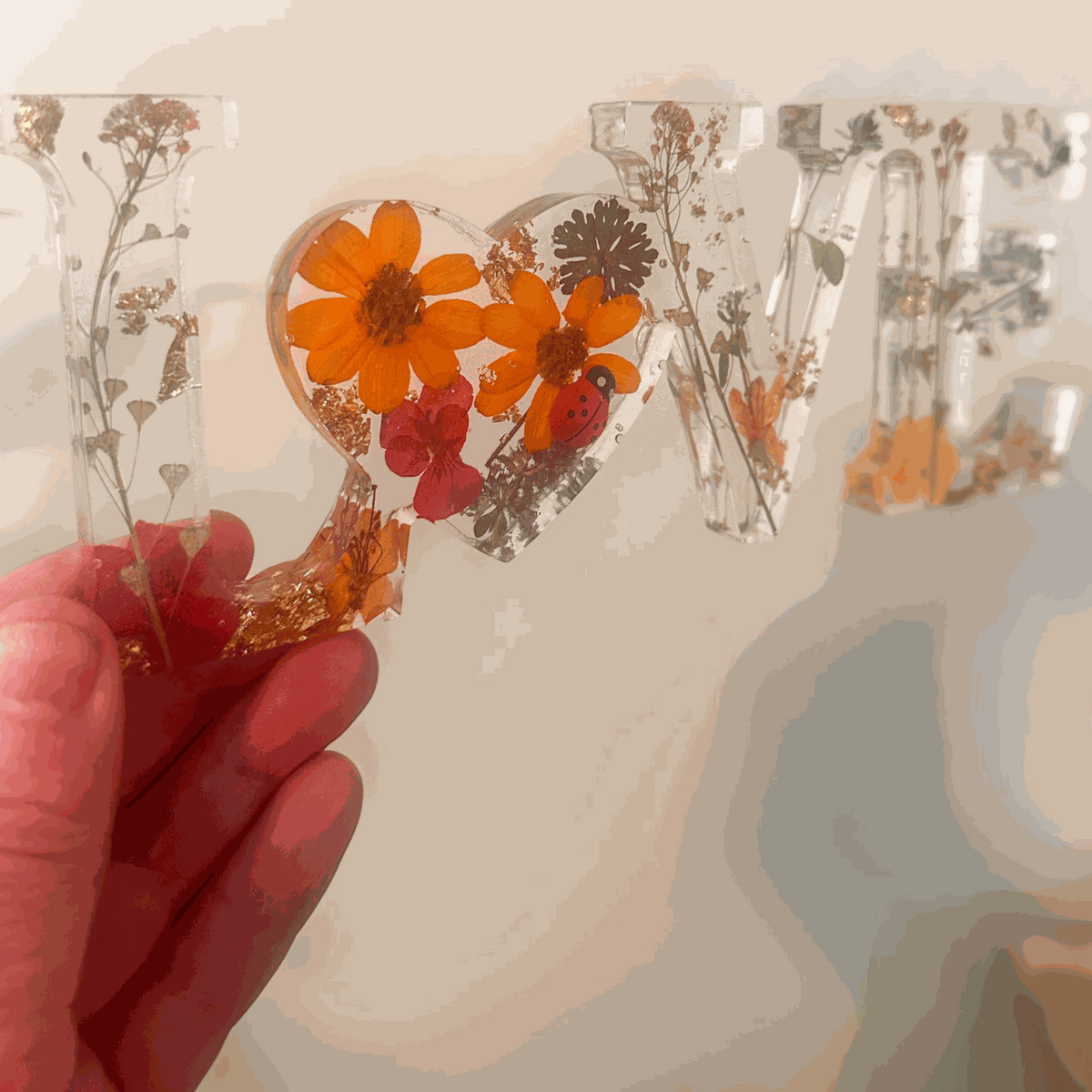 Pressed flower resin decor spelling LOVE with real wildflowers and a tiny ladybug inside clear resin letters