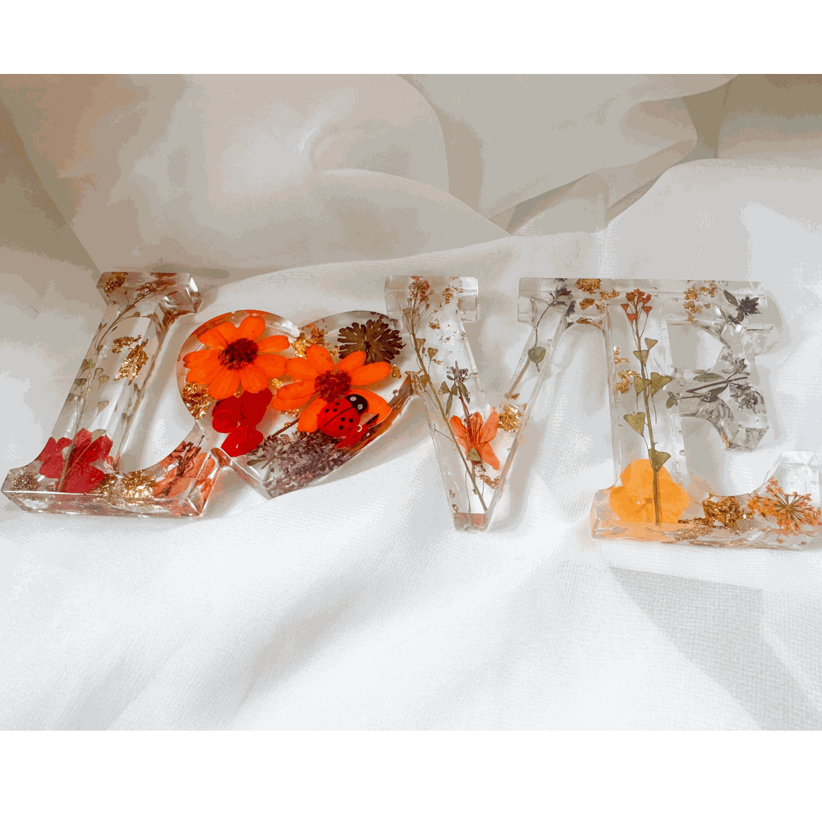Pressed flower resin decor spelling LOVE with real orange and red blooms and a tiny ladybug inside clear resin letters