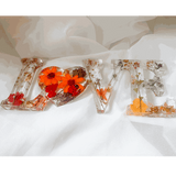 Pressed flower resin decor spelling LOVE with real orange and red blooms and a tiny ladybug inside clear resin letters
