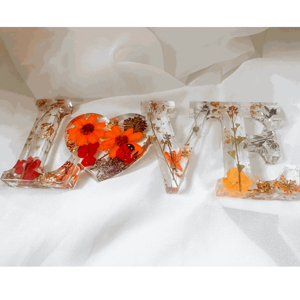 Pressed flower resin decor spelling LOVE with real orange and red blooms and a tiny ladybug inside clear resin letters