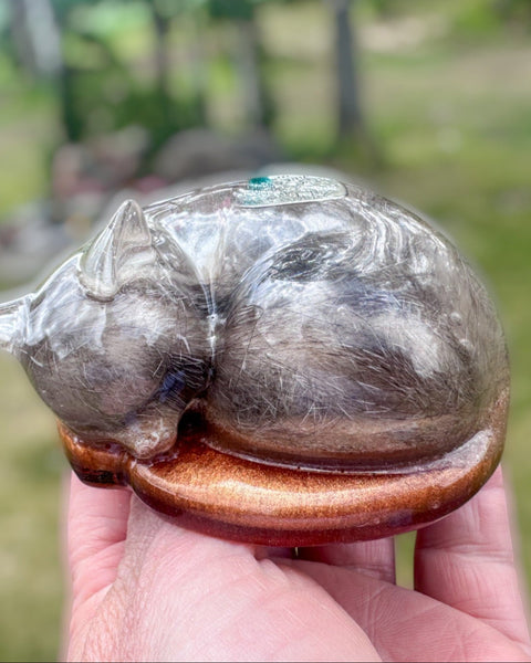 Crystal cat figurine held in a hand with a blurred outdoor background