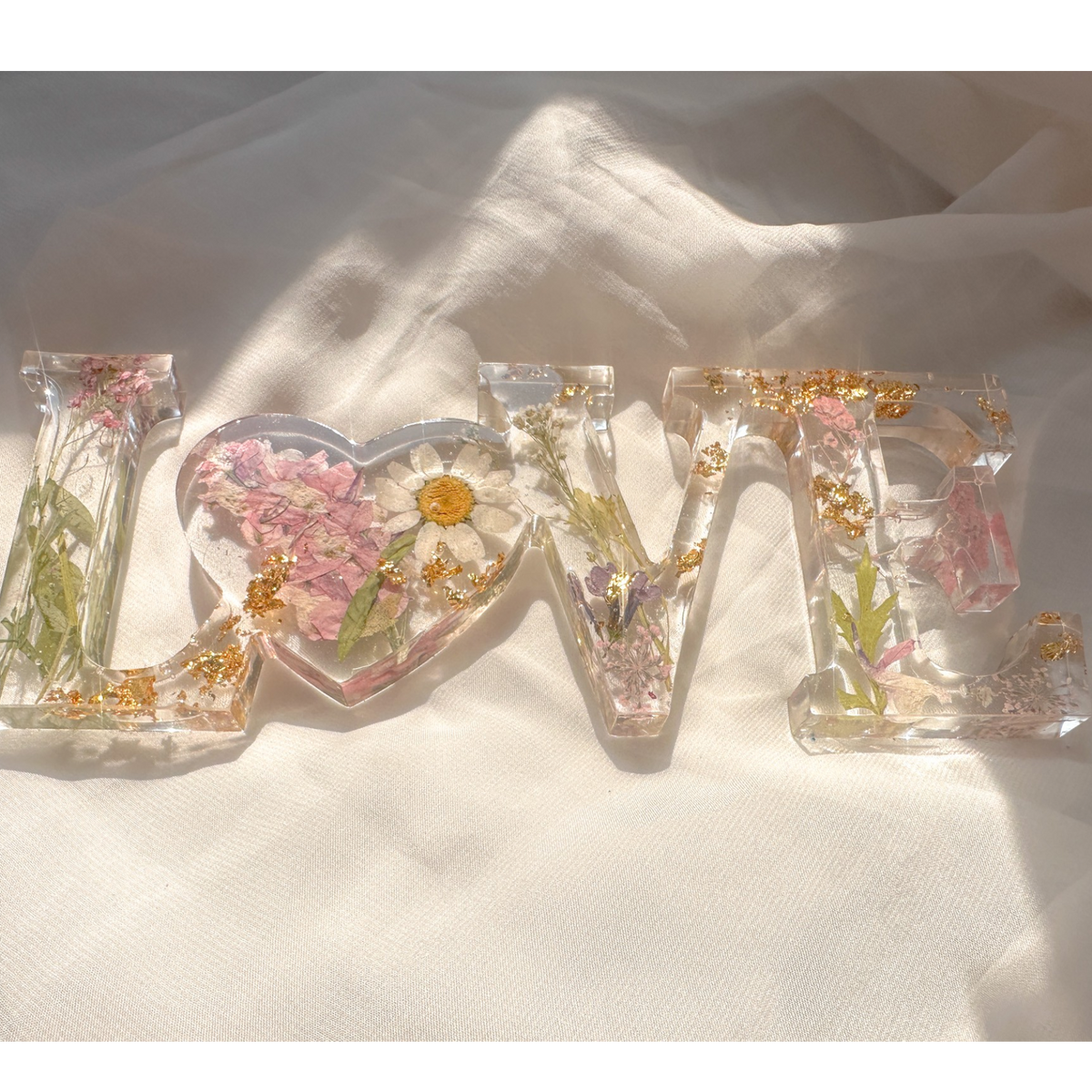 Daisy resin word artwith pressed white daisy, blush blooms, gold leaf flakes, and heart-shaped O design