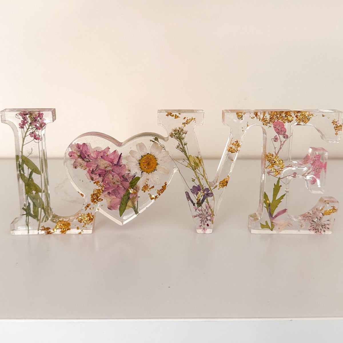 Daisy resin word artwith real pressed white daisy and blush blooms, gold leaf flakes, and heart-shaped O design
