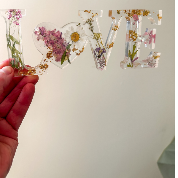 Daisy resin word artfeaturing real pressed white daisy and blush blooms with gold leaf flakes and heart-shaped O design