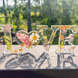 Daisy resin word art with pressed white daisy, blush blooms, and gold leaf flakes in heart-shaped O design