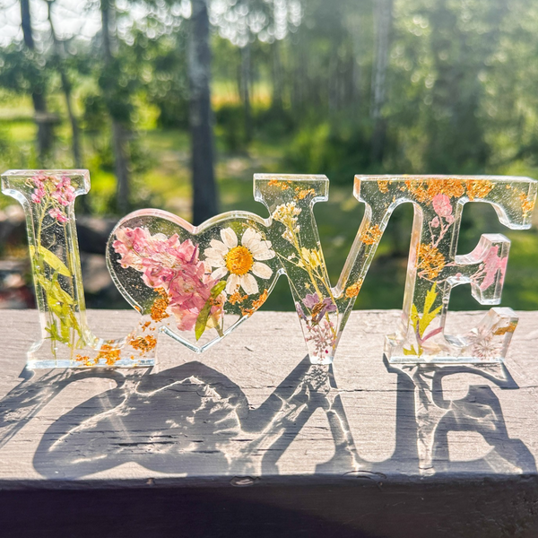 Daisy resin word art with pressed white daisy, blush blooms, and gold leaf flakes in heart-shaped O design
