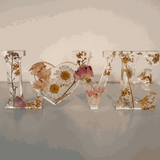 Whispering Meadow LOVE resin word art with white daisies, pink and purple wildflowers, gold leaf flakes, and bunny tail accents