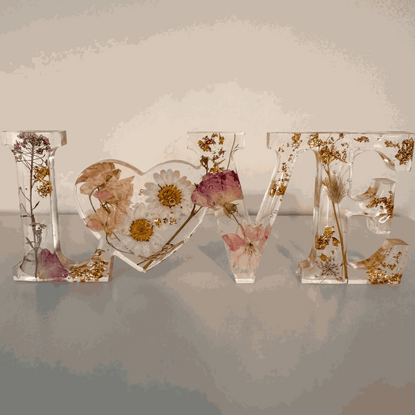 Whispering Meadow LOVE resin word art with white daisies, pink and purple wildflowers, gold leaf flakes, and bunny tail accents