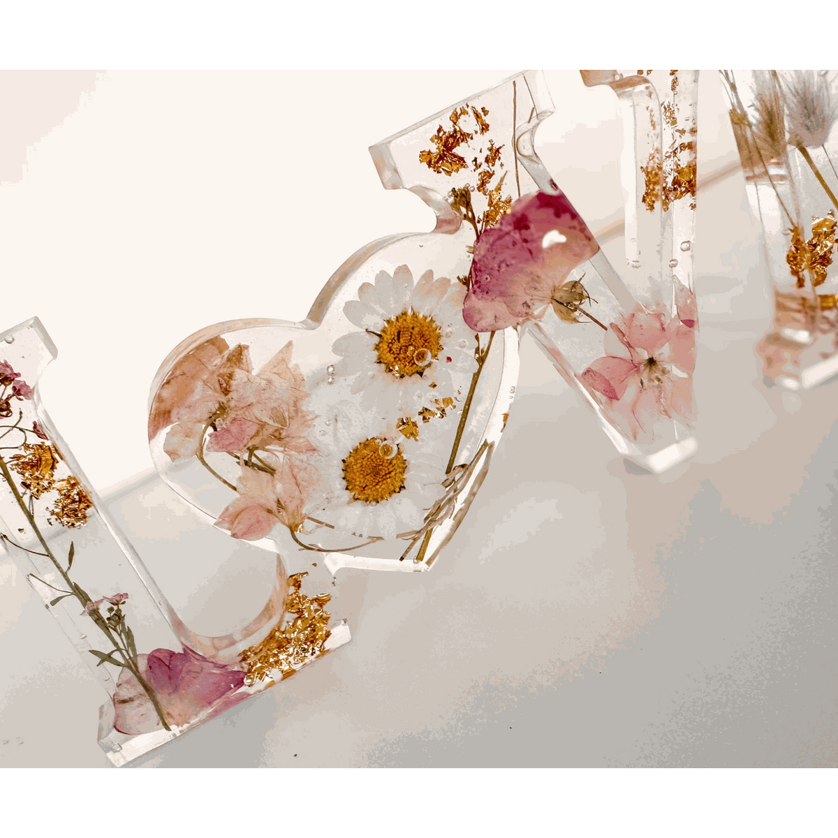 Whispering Meadow LOVE resin word art with white daisies, pink and purple wildflowers, bunny tail accent, and gold leaf flakes