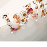 Whispering Meadow LOVE resin word art with white daisies, pink and purple wildflowers, bunny tail, and gold leaf flakes