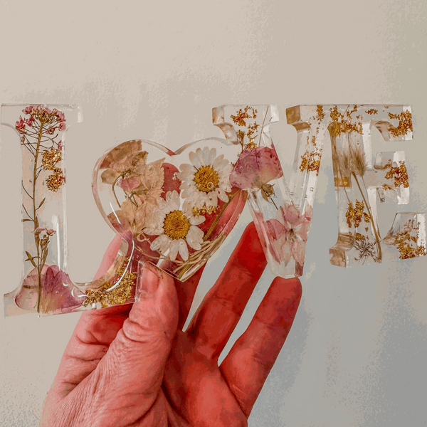 Whispering Meadow LOVE resin word art with white daisies, pink and purple wildflowers, gold leaf, and bunny tail accents