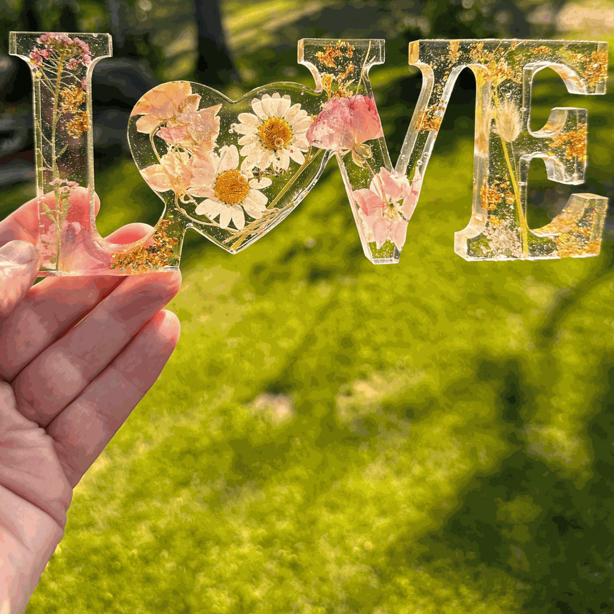 Whispering Meadow LOVE resin word art with white daisies, pink and purple wildflowers, gold leaf flakes, and a bunny tail accent