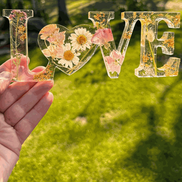 Whispering Meadow LOVE resin word art with white daisies, pink and purple wildflowers, gold leaf flakes, and a bunny tail accent
