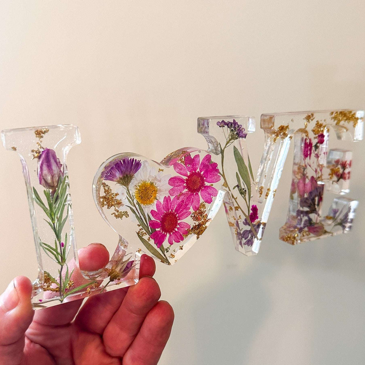 Wildflower resin word art with pink daisies, purple wildflowers, rose buds, and gold leaf accents spelling LOVE