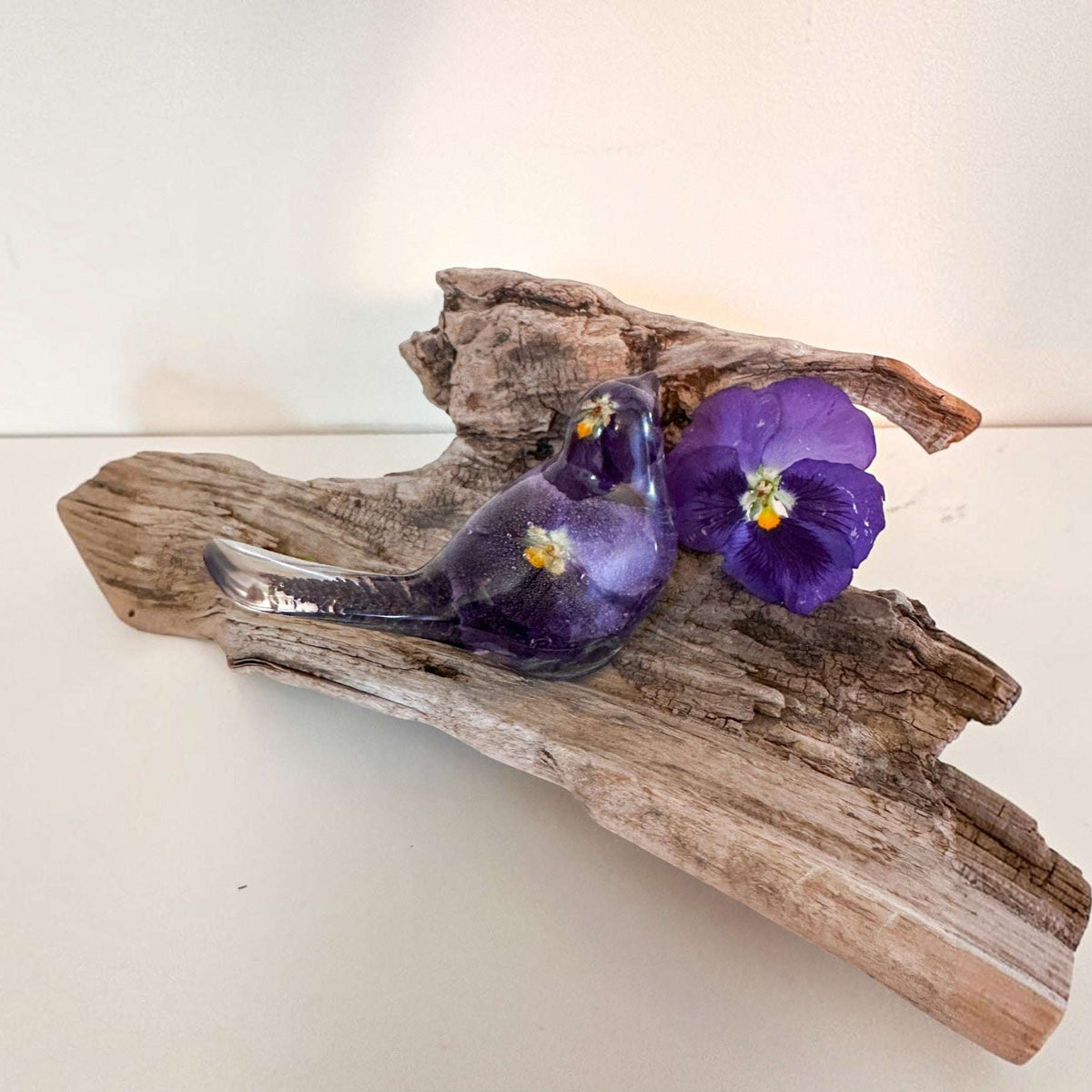Purple Pansy resin bird decor piece with embedded real pressed purple pansy flowers, clear glossy finish, perched on driftwood.