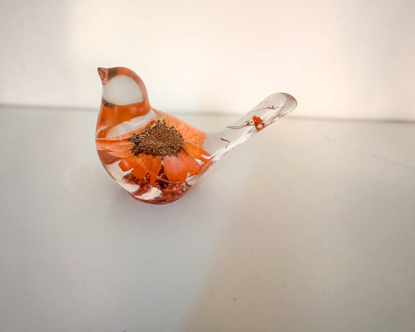 Resin bird decor with orange sunflower encased inside, clear tail featuring small flower accents, and copper leaf base shimmer.